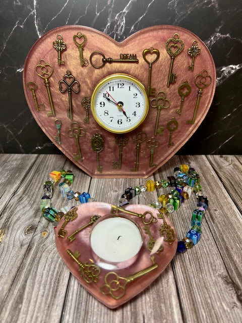 This handcrafted pink resin heart clock features vintage keys, adding a touch of timeless charm. Choose between a star votive or a heart votive, each adorned with matching vintage keys.

Dimensions: 7.87" x 9.84" x 0.71" (W x H)
Approximate Weight: 3 lbs

A unique and elegant piece, perfect for any space or as a thoughtful gift.